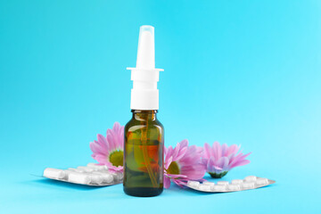 Allergy treatment. Nasal spray, pills and flowers on light blue background