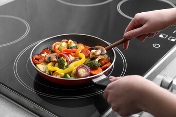Woman cooking vegetables and mushrooms in frying pan on cooktop indoors, closeup