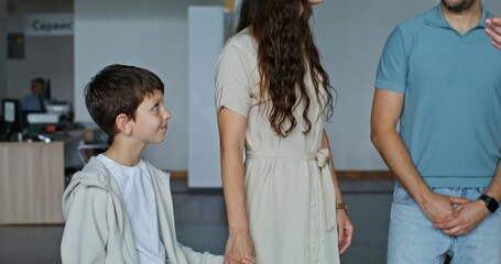 Fototapeta premium The car dealership manager shows cars to customers standing in the showroom. A family with a child chooses a car
