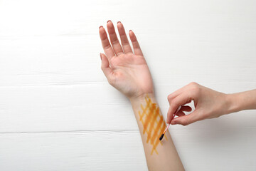 Woman applying topical iodine with cotton swab on hand at white wooden table, top view
