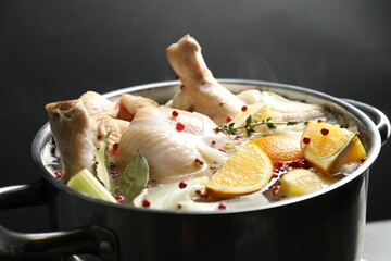 Whole fresh turkey, cut citrus fruits and spices boiling in pot on black background, closeup
