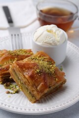 Delicious baklava with crushed nuts and ice cream on grey table, closeup