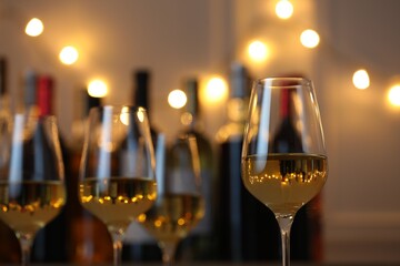 Tasty white wine in glasses against blurred background with festive lights, closeup. Bokeh effect