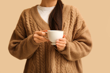 Young Asian woman with cup of hot tea on beige background, closeup