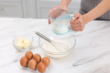 Woman adding flour into bowl with dough at white marble table, closeup
