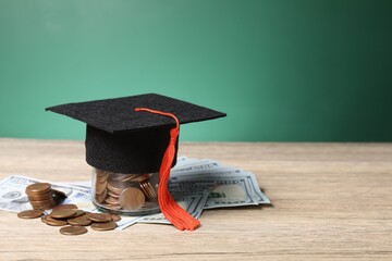 Tuition payment. Graduate hat, dollar banknotes and coins on wooden table, closeup. Space for text