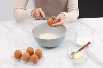 Making dough. Woman adding egg into bowl at white marble table, closeup