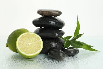 Spa composition with limes, massage stones and green leaves on wet surface against white background