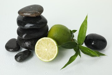 Spa composition with limes, massage stones and green leaves on wet surface against white background