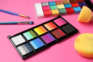 Bright face paints, brushes and sponges on pink background, closeup
