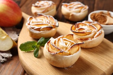 Tasty apple roses with powdered sugar served on wooden table, closeup