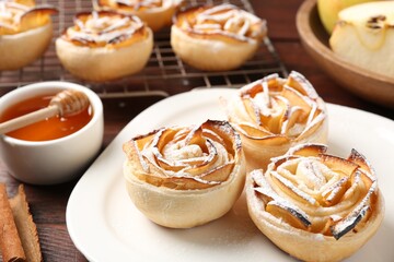 Tasty apple roses with powdered sugar served on wooden table, closeup