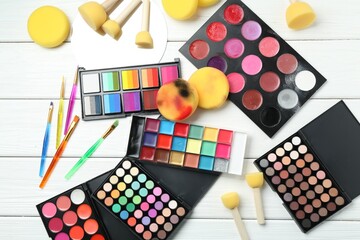 Face paints, tools and makeup products on white wooden background, flat lay