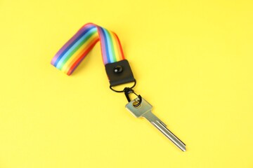Key with keychain in LGBT colors on yellow background, closeup