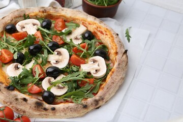 Tasty pizza with cherry tomatoes, black olives, mushrooms and arugula on white tiled table, closeup. Space for text