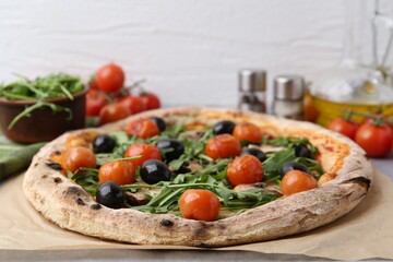 Tasty pizza with cherry tomatoes, black olives, mushrooms and arugula on table, closeup