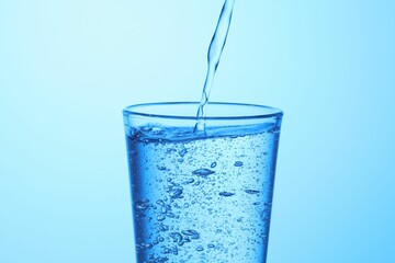Pouring soda water into glass on light blue background, closeup