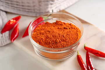 Glass bowl with red chili powder and peppers on white background
