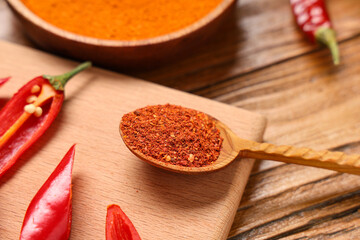 Spoon with red chili flakes and peppers on wooden background, closeup