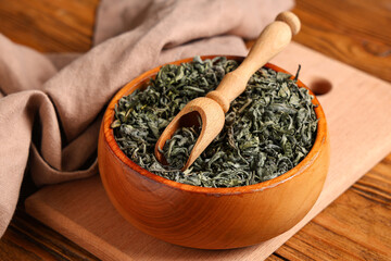 Bowl and scoop with dried green tea leaves on wooden background