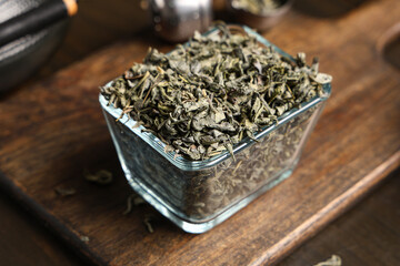 Glass bowl with dried green tea leaves on wooden background