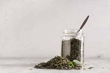 Jar with dried green tea leaves on white background