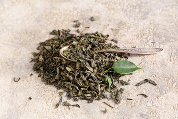 Teaspoon with dried green tea leaves on white background