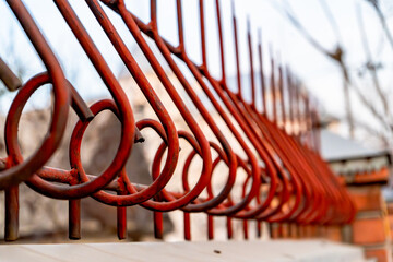 A close-up of a red metal fence with intricate circular and angular patterns. The rusted surface and peeling paint highlight the texture and weathered condition of the structure. 