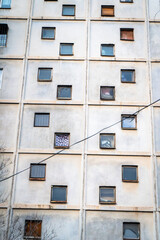 A close-up view of a Soviet-era apartment building featuring a repetitive grid of small, square windows. The building’s facade shows signs of age, with peeling paint, discoloration, and rust stains. 