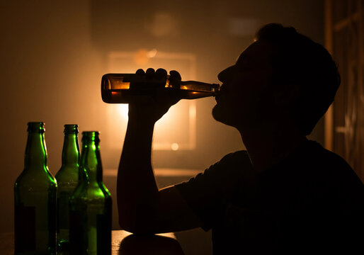 Side Profile of a Man Drinking Beer: A side profile captures a man enjoying a beer from a bottle, with soft light enhancing the relaxed vibe in a casual setting.