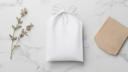 Minimalist flatlay featuring a white drawstring pouch, dried flowers, and a textured stone on a marble background. Simple elegance.