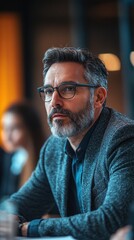 Obraz premium A man with a beard and glasses, dressed in business attire, leading a meeting in a modern conference room with colleagues.