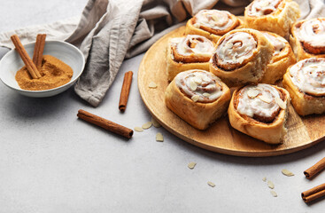 Freshly baked cinnamon rolls with icing and almond flakes on wooden tray