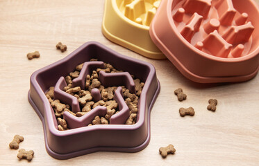 Slow feeding bowl containing dry pet food on wooden table