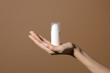 Woman's hand gently hold white bottle of unmarked cosmetics. Mockup container with dispenser for serum, lotion, cream, and retinol.