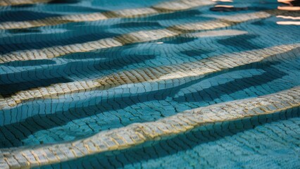 Obraz premium Textured reflections of gold patterns shimmering on a blue water surface in a pool with geometric tile layouts in horizontal alignment.