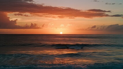 Obraz premium Vibrant golden sunset reflecting on calm ocean waves with soft clouds in pink and orange hues, sun positioned at horizon creating serene ambiance.