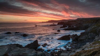 Obraz premium Dramatic rocky coastline at sunset with vibrant oranges and purples in the sky reflecting on calm waves creating a serene seascape scene