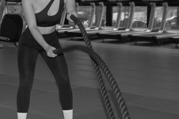 portrait beautiful young woman in fitness style at exercise class indoor with battle ropes....