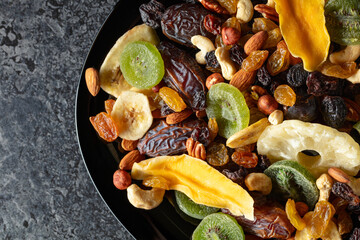 Dried tropical fruits, nuts, and raisins in black plate.
