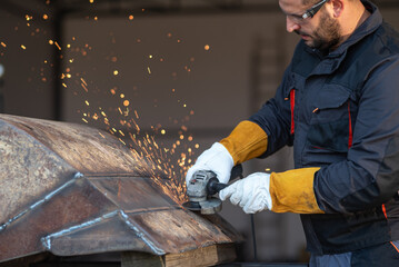 Metal worker using angle grinder producing sparks during polishing metal structure