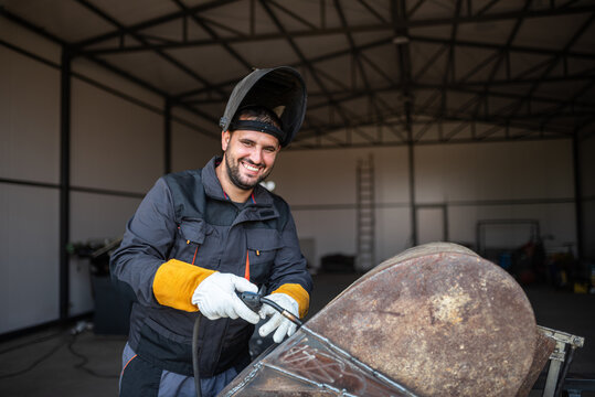 Metal worker smiling and holding welding torch in factory