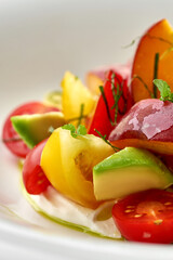 A vibrant and refreshing summer salad featuring ripe tomatoes, creamy avocado, and sweet peaches. The salad is tossed in a light vinaigrette and served on a bed of fresh greens.