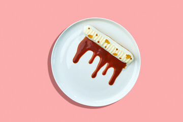 A classic eclair dessert, filled with creamy custard and topped with a drizzle of rich caramel sauce. The eclair is presented on a white plate