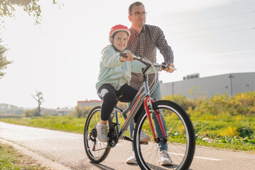Fototapeta premium Father teaching daughter riding bicycle on bike path