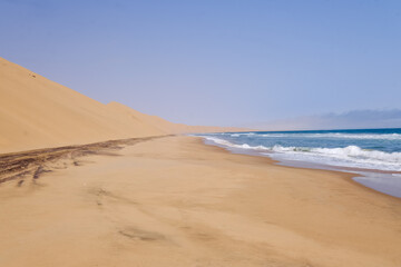 A breathtaking view of Sandwich Harbour, where golden sand dunes meet the deep blue Atlantic Ocean, creating a stunning contrast in this remote and untouched landscape.