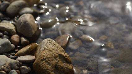 Smooth river stones submerged in clear shallow water with sunlight reflections