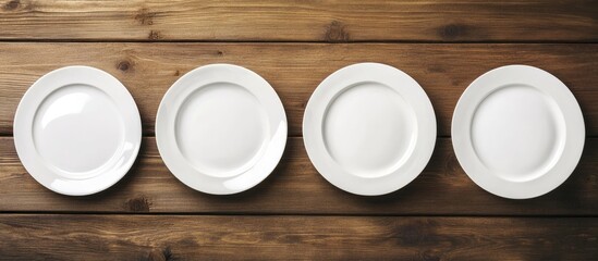 Top view of four white empty plates arranged neatly in a row on a rustic wooden table, showcasing their simple design and elegant layout