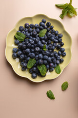 Dish with fresh blueberries and mint leaves on a beige background. Elegant and vibrant fruit composition. Concept of healthy eating and freshness