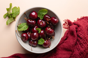 Close-up of a bowl of bright cherries with fresh mint and red fabric on neutral background seen from above. Concept of freshness and nutrition